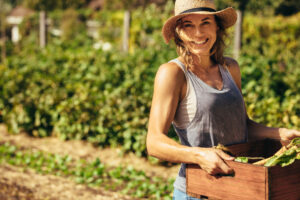 Enjoying the Freedom and Self-Sufficiency Woman Smiling in the Garden Carrying a box of vegetables