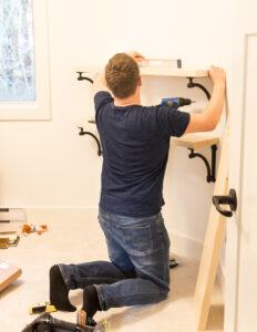 Man measuring wood to cut DIY Wooden Frames Guy Installing Shelves